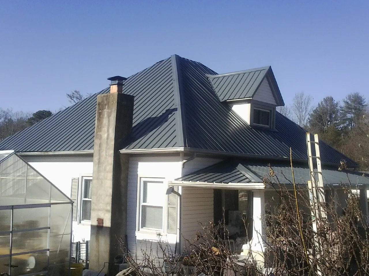 Dark blue standing seam metal roof on a white farmhouse with dormer — Slate & Tile Roof Repair by Roofing Brothers in Mondamin