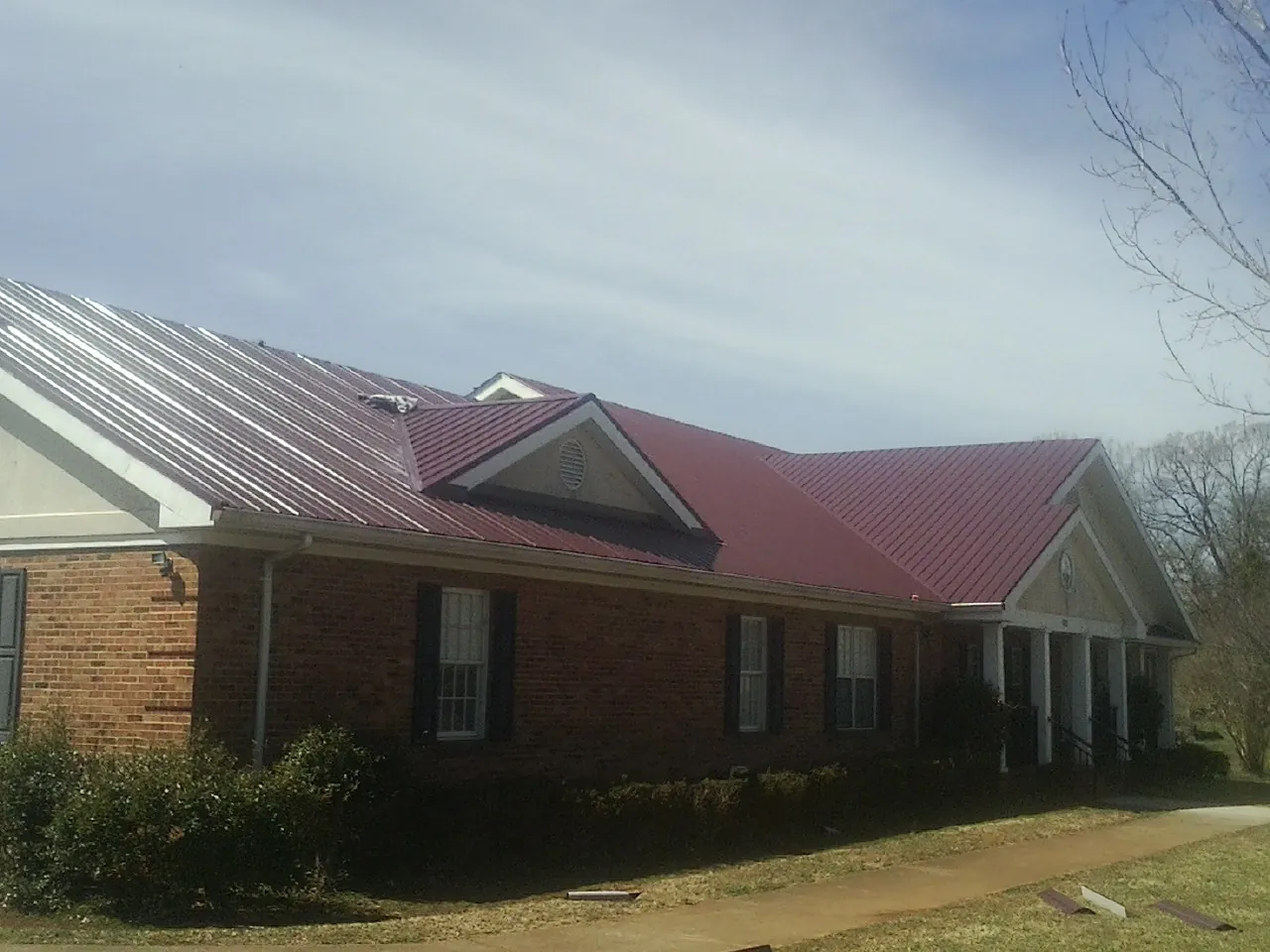 Red metal roof with gabled entries on a long brick building, from a Hail Damage Roof Repair job in Mondamin