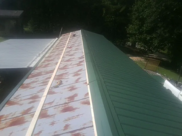 Old rusted panels beside newly installed green metal roofing — Wind Damage Roof Repair by Roofing Brothers in Mondamin