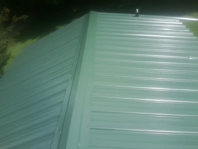 New green metal panels meeting at the ridge of a roof — Flat Roof Repair work by our crew in Mondamin