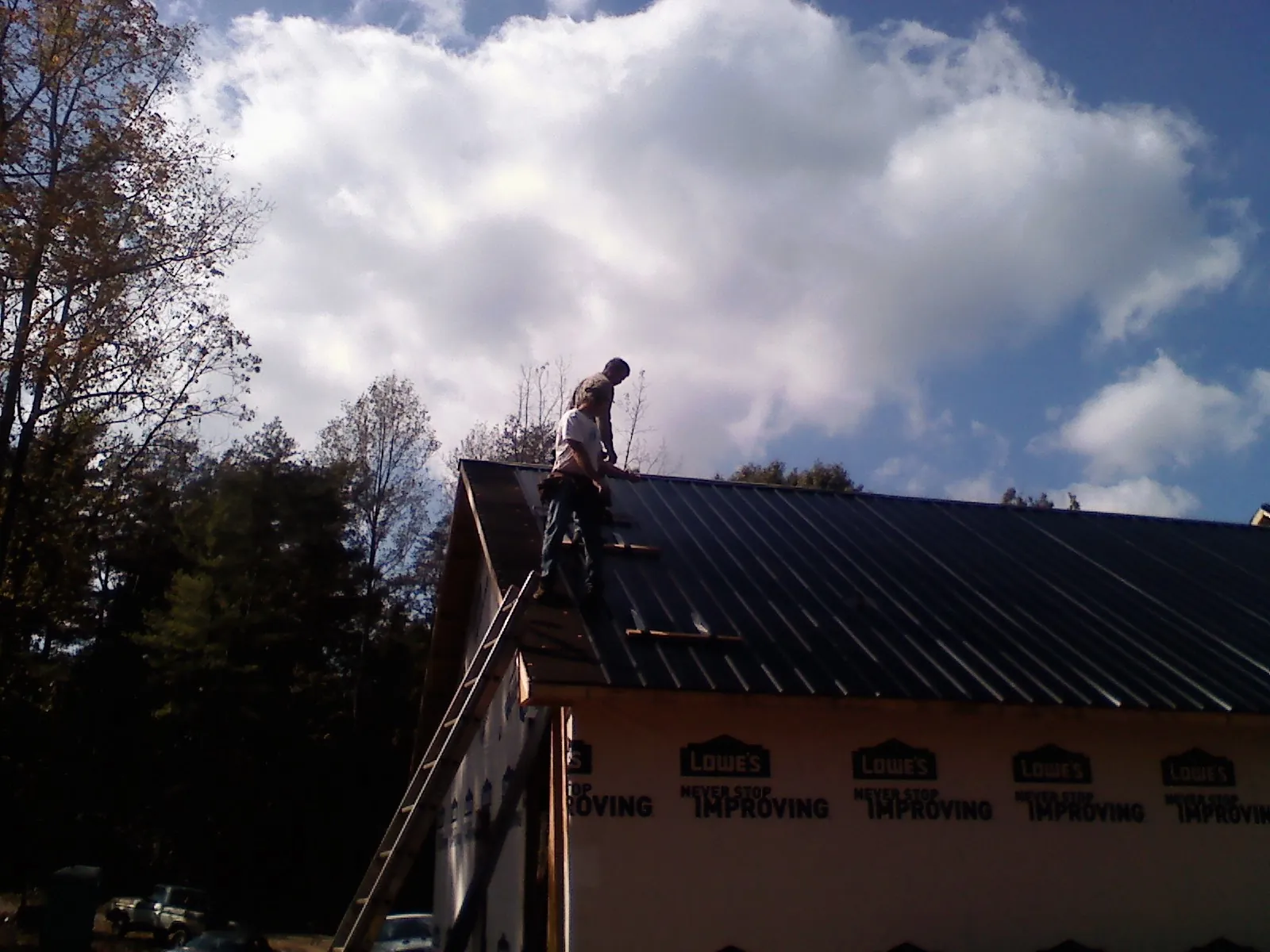 Roofer fastening dark metal panels high against a cloudy sky, from a Roof Inspection job in Mondamin