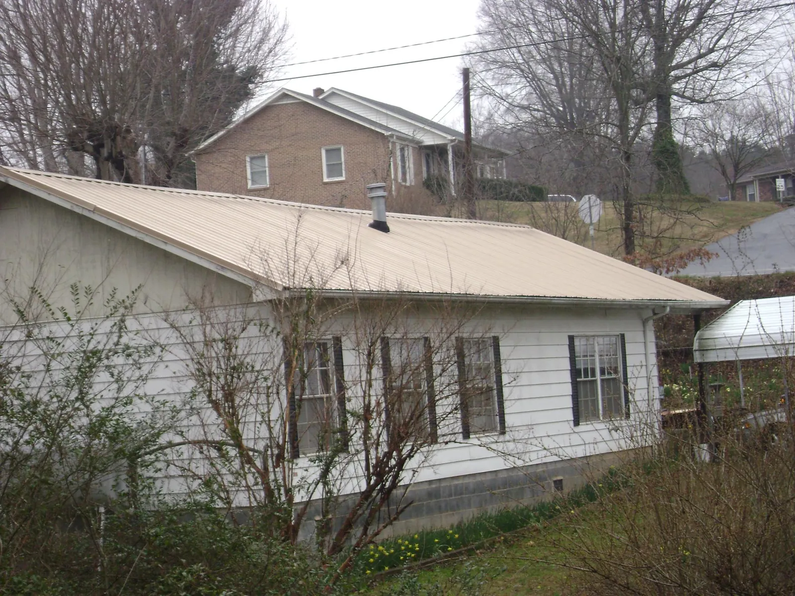 Tan metal roof on a white sided house set into a hillside — Commercial Roofing by Roofing Brothers in Mondamin